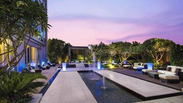 A modern outdoor lounge area with a pool, seating, and a building in the background.