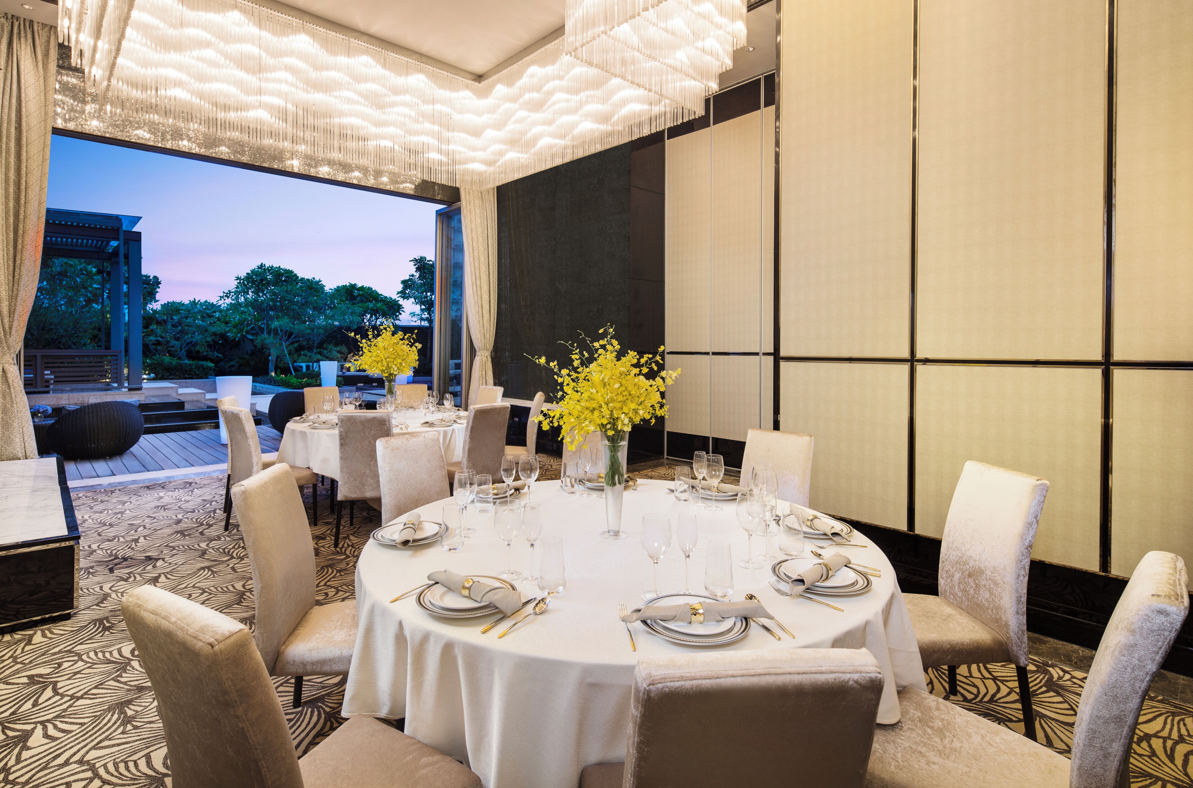 A dining area with round tables, chairs, and a vase of yellow flowers.