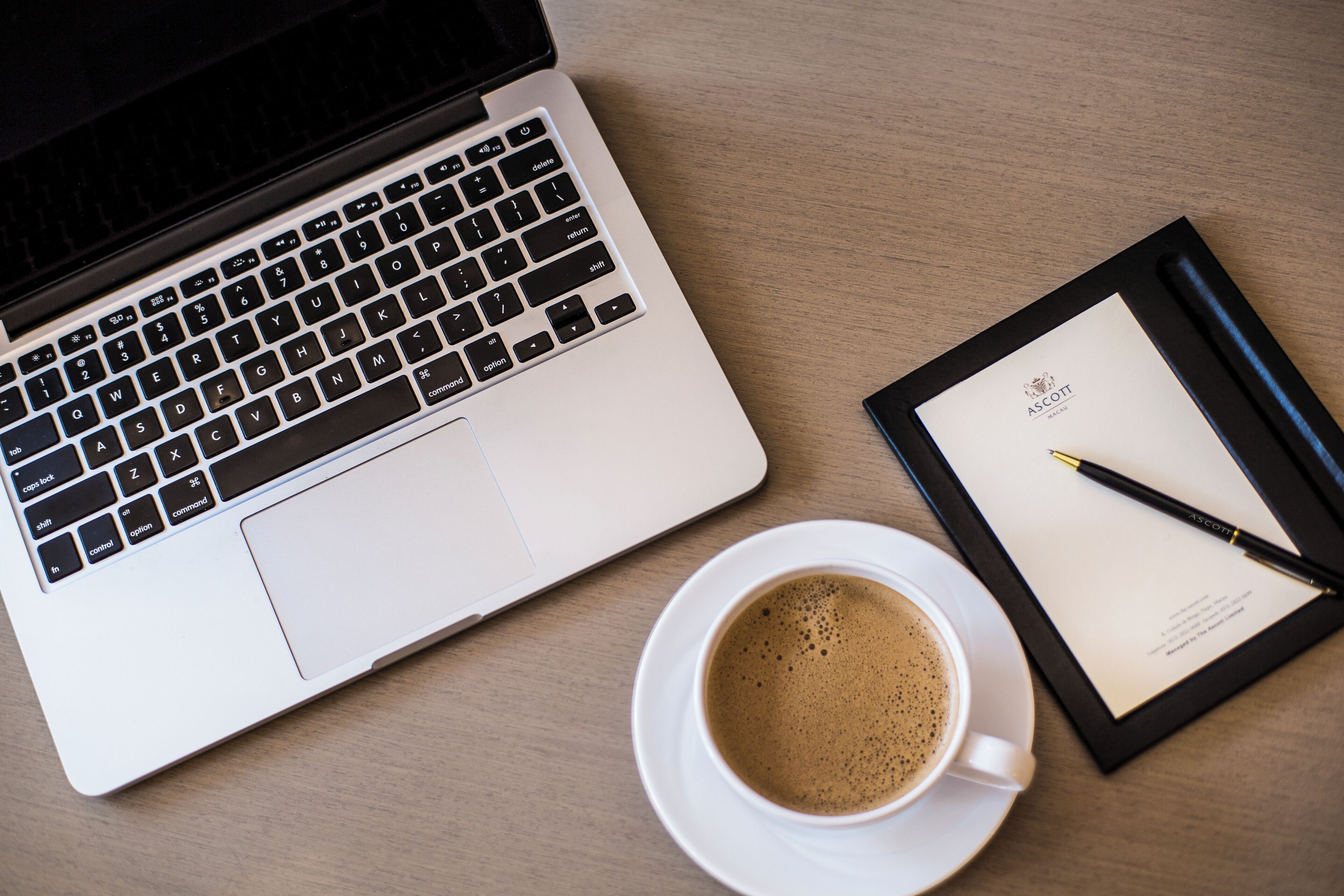 A laptop, a cup of coffee, a pen, and a framed document on a wooden surface.