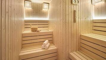 A sauna with wooden benches, a bench with towels, a wooden bucket, and a wall-mounted thermometer.