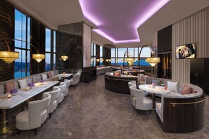 Een moderne hotel lobby met een bar, zitgedeeltes en grote ramen met uitzicht op de stad.