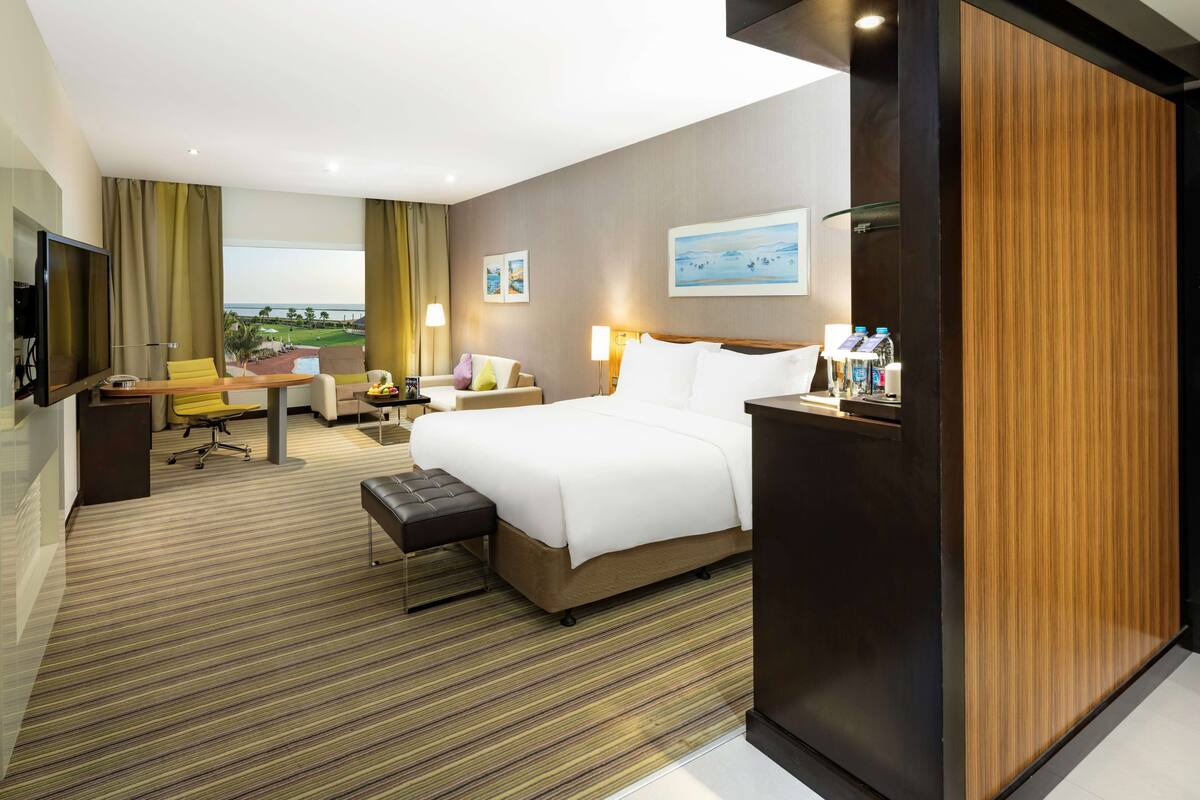 A hotel room with a large bed, a desk, a chair, a TV, and a view of the outdoors.