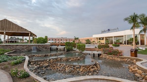 A landscaped area with a water feature, a covered seating area, and a building with a sign. - Radisson Blu Resort, Jizan (Jizan)