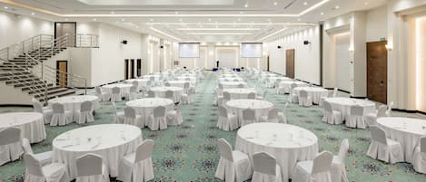 Un amplio salón de conferencias con varias mesas redondas, sillas blancas y suelo alfombrado.