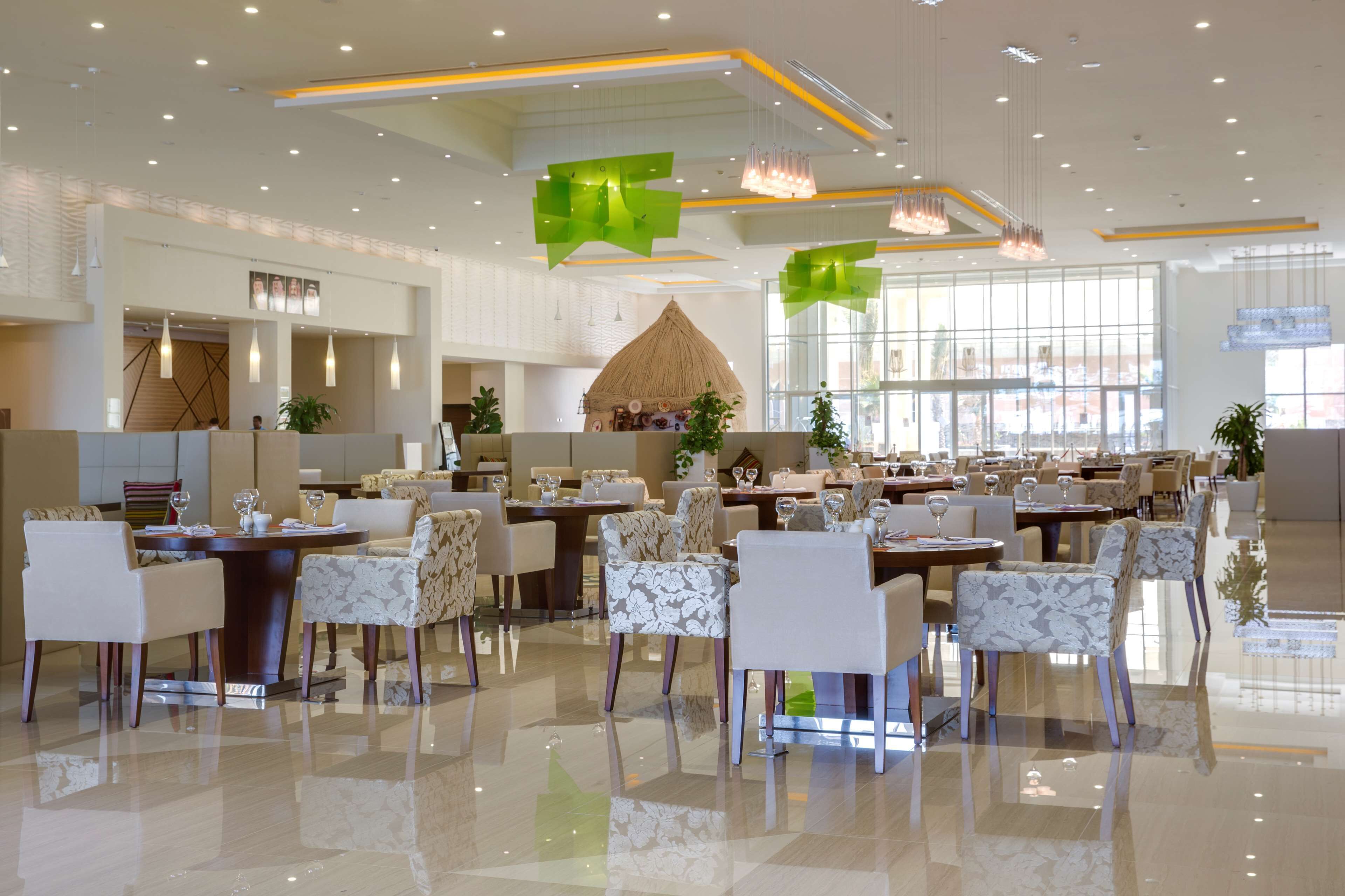 Un amplio vestíbulo de hotel con varias zonas de comedor, una recepción y un gran ventanal que proporciona luz natural.