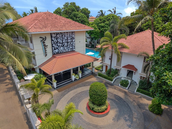 A multi-story building with a tiled roof, a covered outdoor seating area, and a landscaped courtyard with a central circular feature.