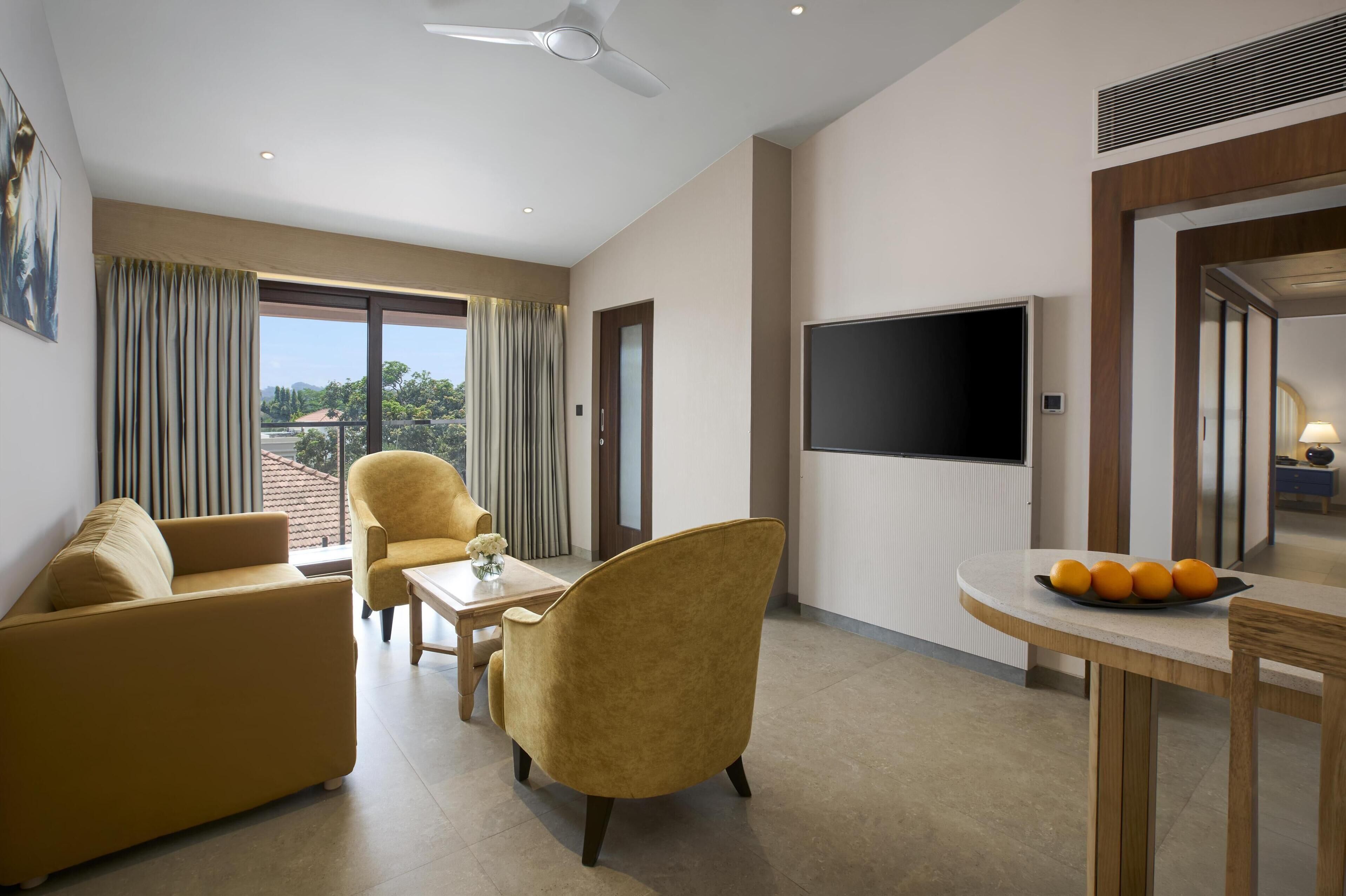 Una habitación de hotel moderna con sofá, sillón, mesa de comedor y televisión de pantalla plana.
