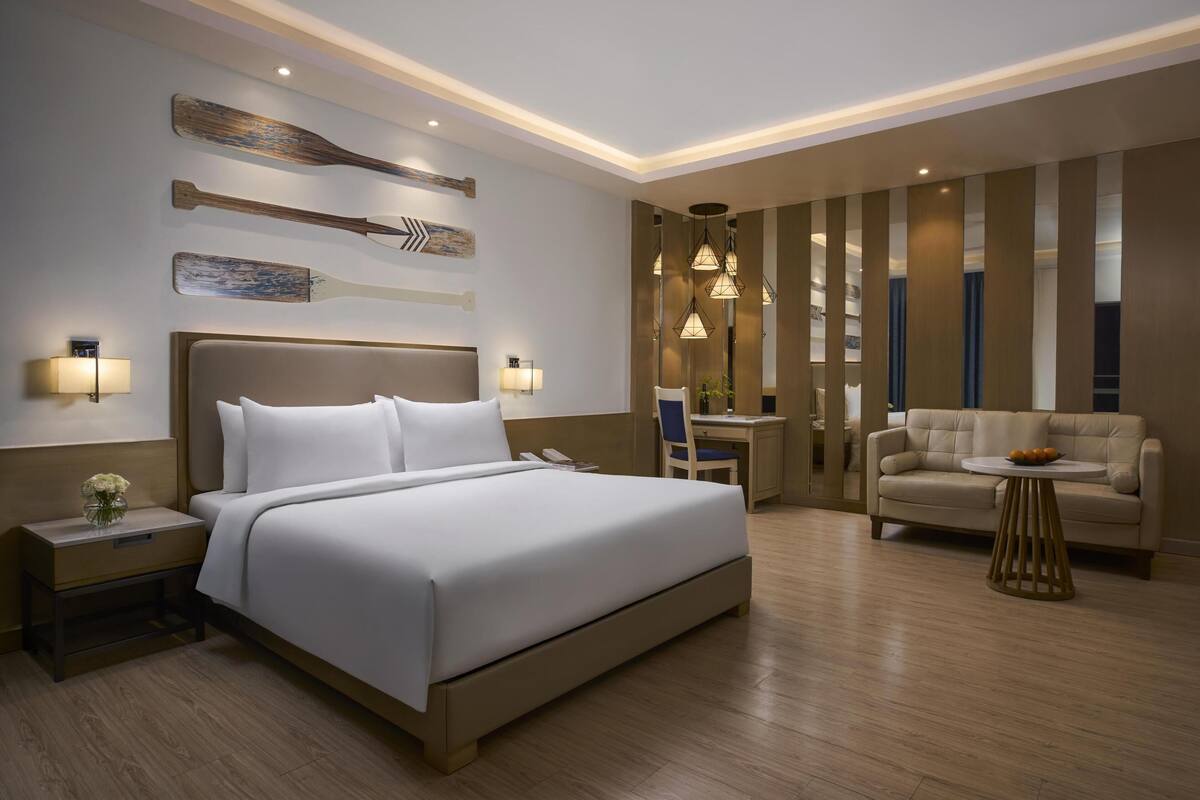 Una habitación de hotel moderna con una cama grande, mesitas de noche, un escritorio, una silla y un sofá.