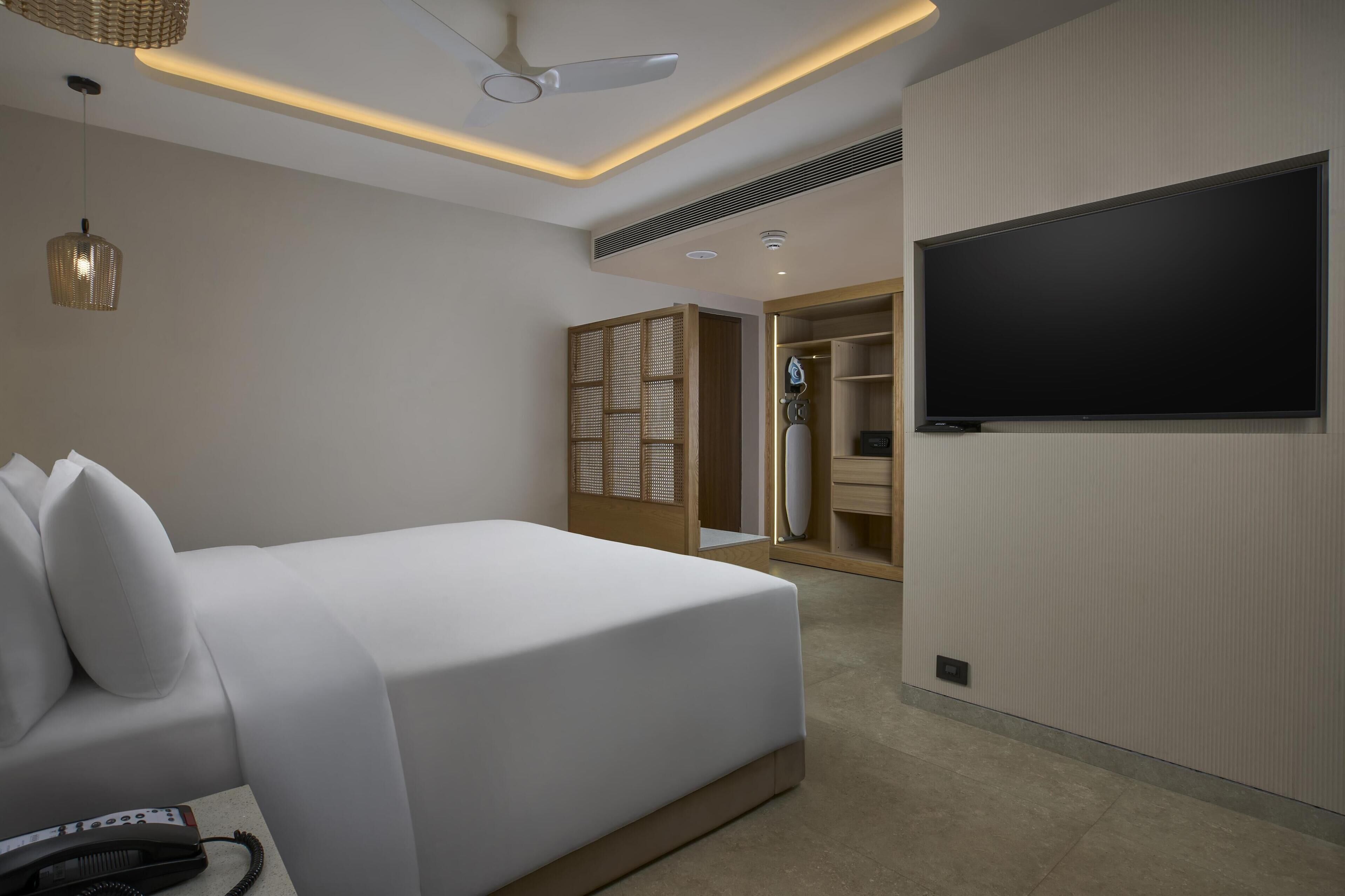 Una habitación de hotel moderna con una cama grande, un televisor de pantalla plana, un ventilador de techo y un vestidor.
