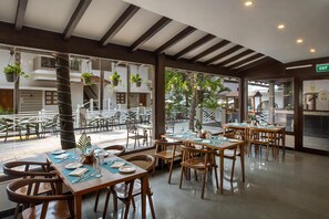 A restaurant with wooden tables and chairs, potted plants, and a view of the outside. - Radisson Goa Candolim (Candolim)