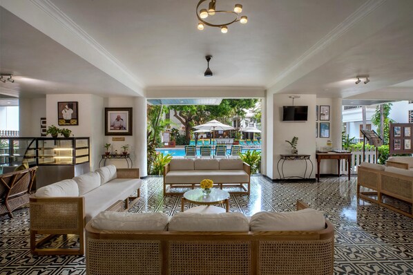 A spacious lobby with a sofa, chairs, a coffee table, and a view of an outdoor pool area. - Radisson Goa Candolim (Candolim)
