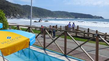 Terraza de madera con vistas a una playa con olas, piscina y un cartel de Apartamentos Vila do Sol.