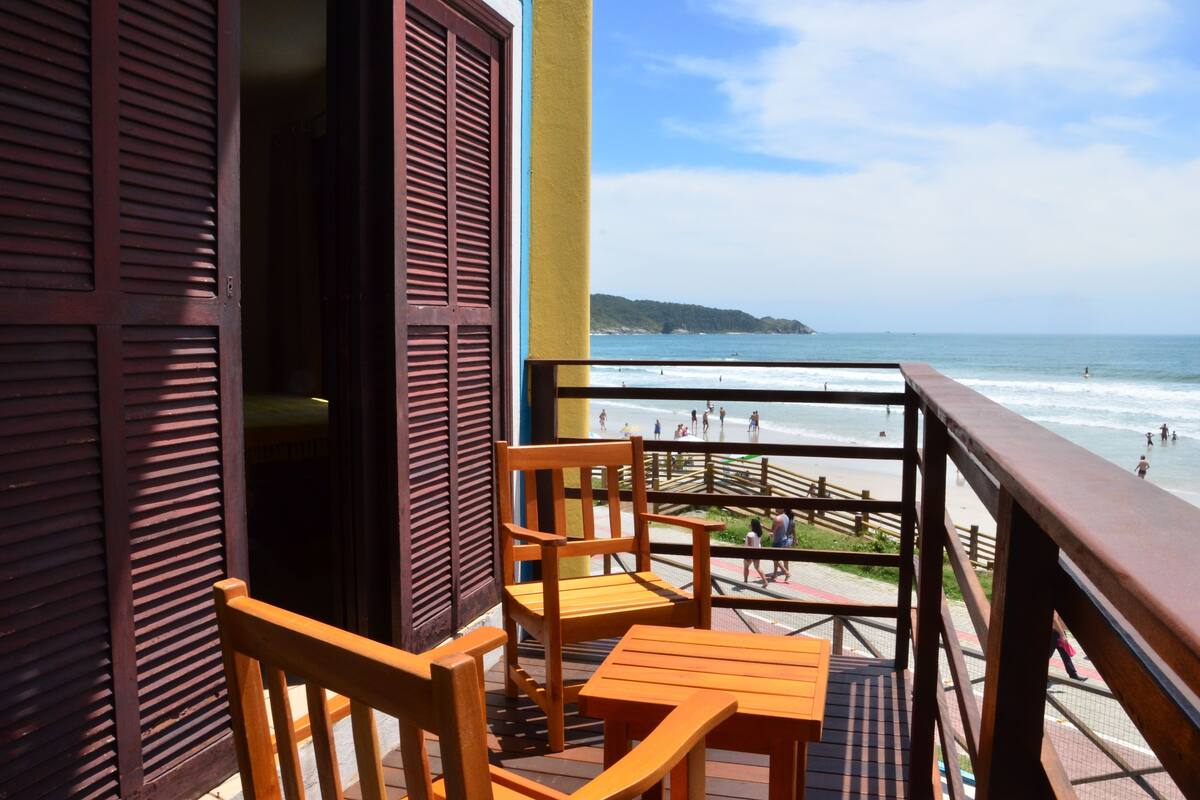 A balcony with wooden furniture, a view of the beach, and a wooden door.
