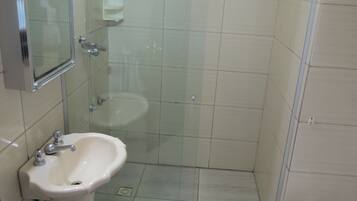 Un baño con ducha de vidrio, lavamanos, inodoro y espejo.