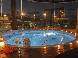 A hot tub with rose petals and candles, surrounded by wooden furniture and a glass enclosure. - Vila do Sol Apartamentos (Bombinhas)