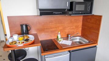 A compact kitchenette with a microwave, sink, and small refrigerator. There are stools and a tray with breakfast items.
