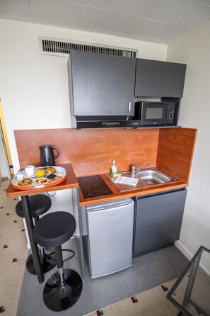 A compact kitchenette with a microwave, sink, and small refrigerator. There are stools and a tray with breakfast items.