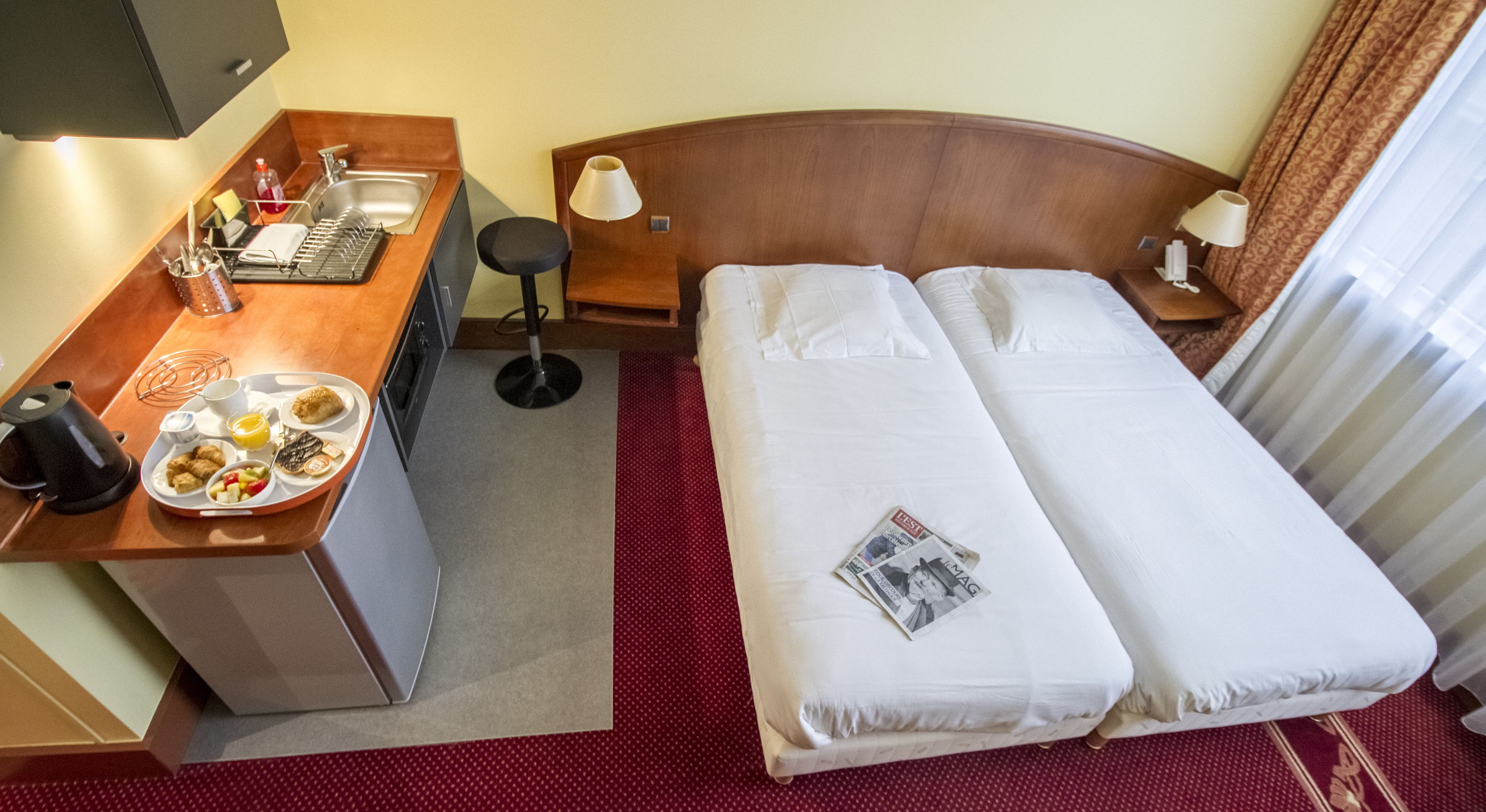 A hotel room with a bed, a desk with a sink, and a breakfast tray.