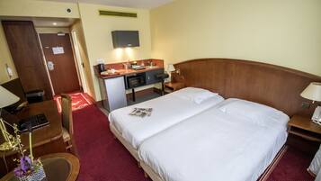 Une chambre d’hôtel avec un grand lit, un bureau avec un ordinateur, une petite kitchenette et un téléviseur fixé au mur.