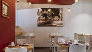 A restaurant interior with tables set for dining, a framed picture on the wall, and hanging light fixtures.