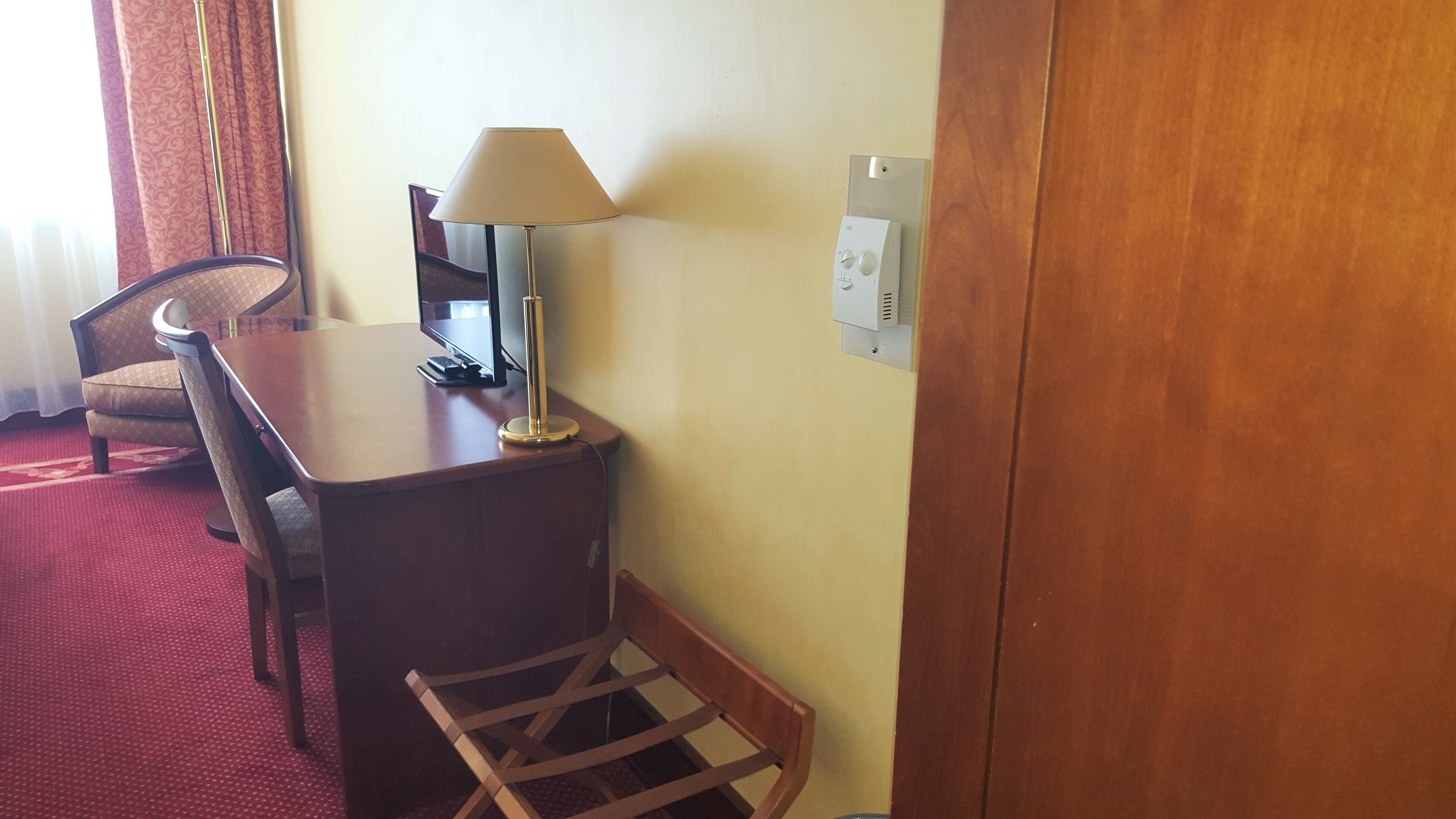 A hotel room with a wooden desk, a lamp, a chair, and a small table.