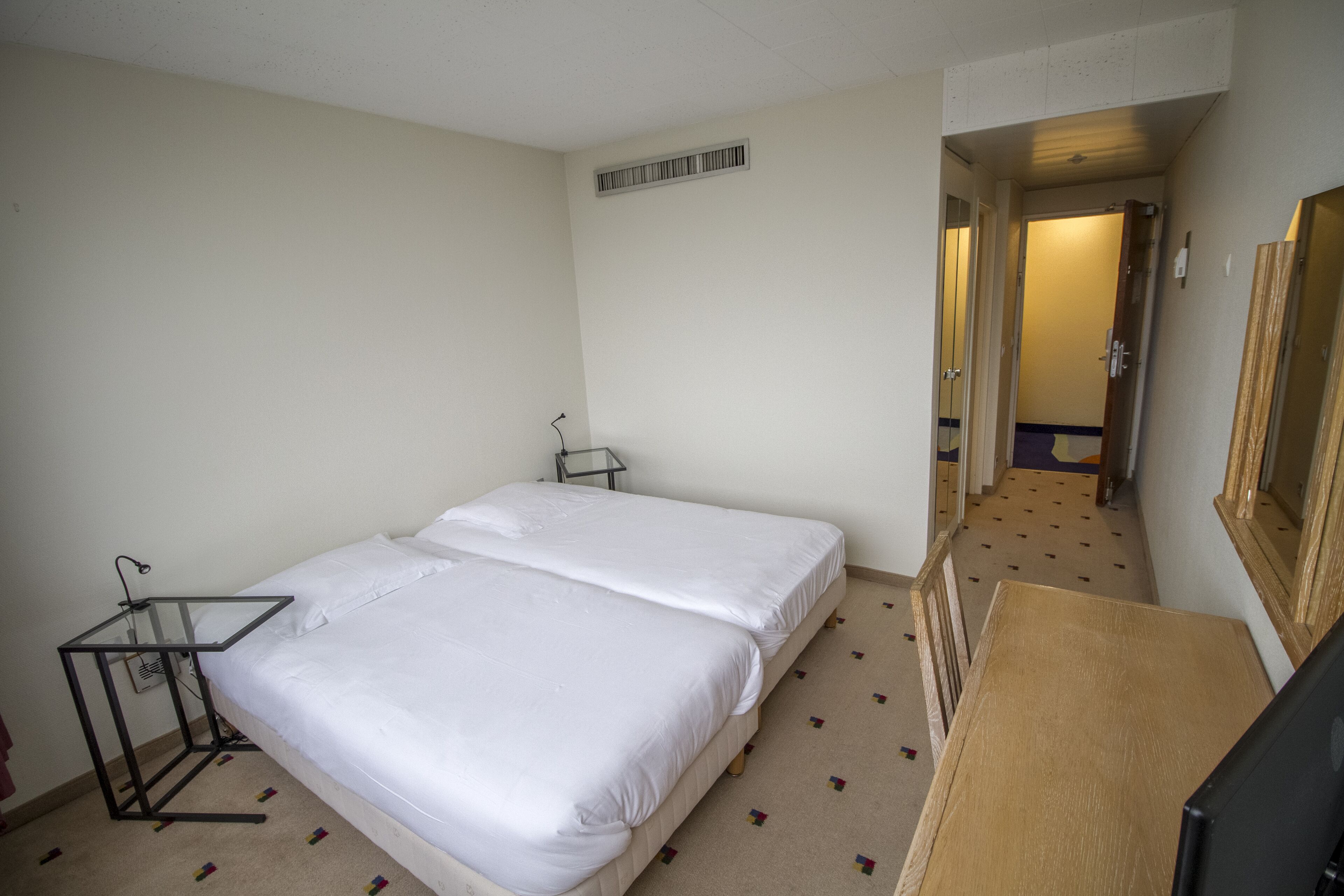 Ein Hotelzimmer mit einem großen Bett, einem Schreibtisch, einem Spiegel und einer Tür zu einem anderen Raum.