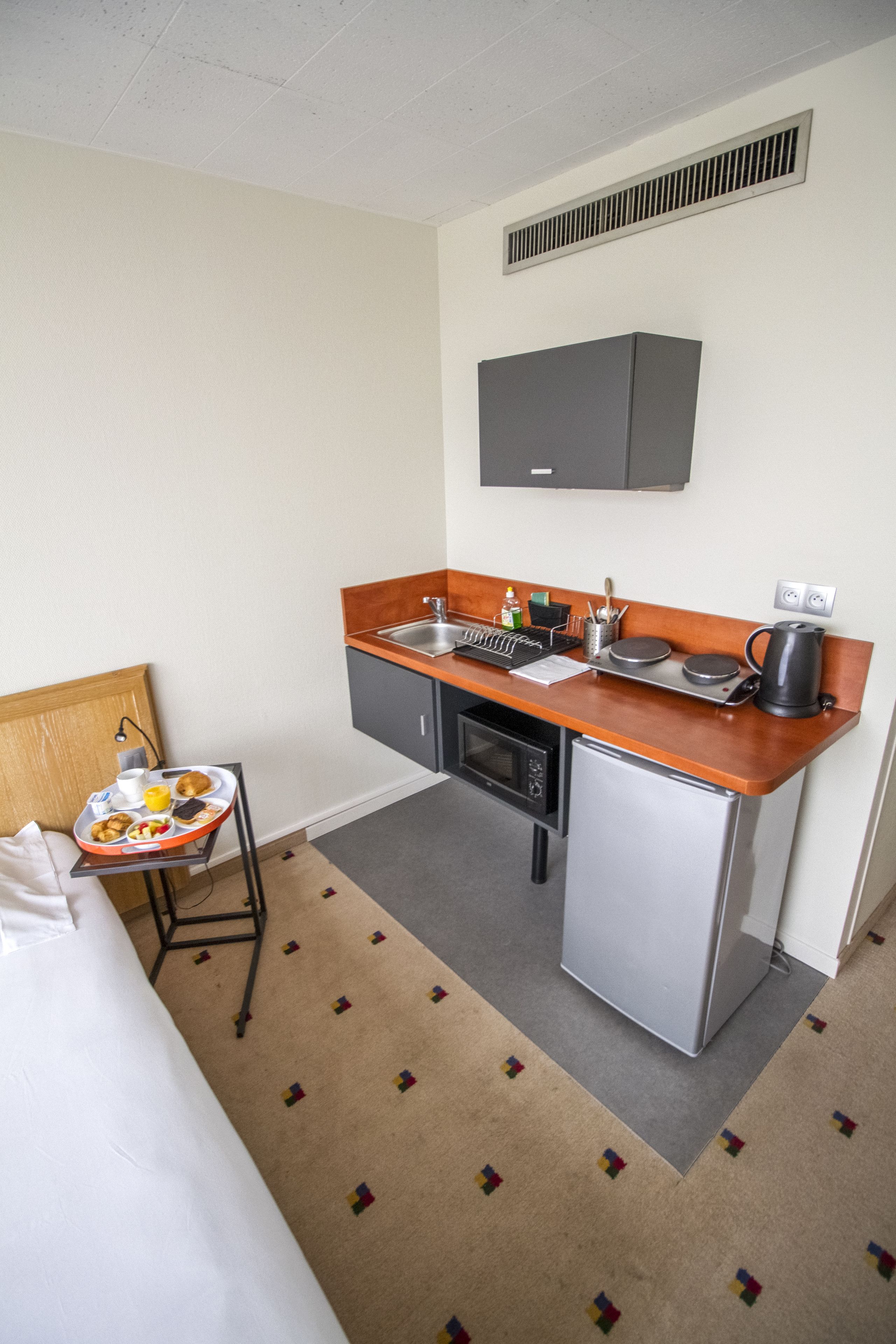 A compact hotel room with a kitchenette, a bed, and a small dining table with breakfast items.