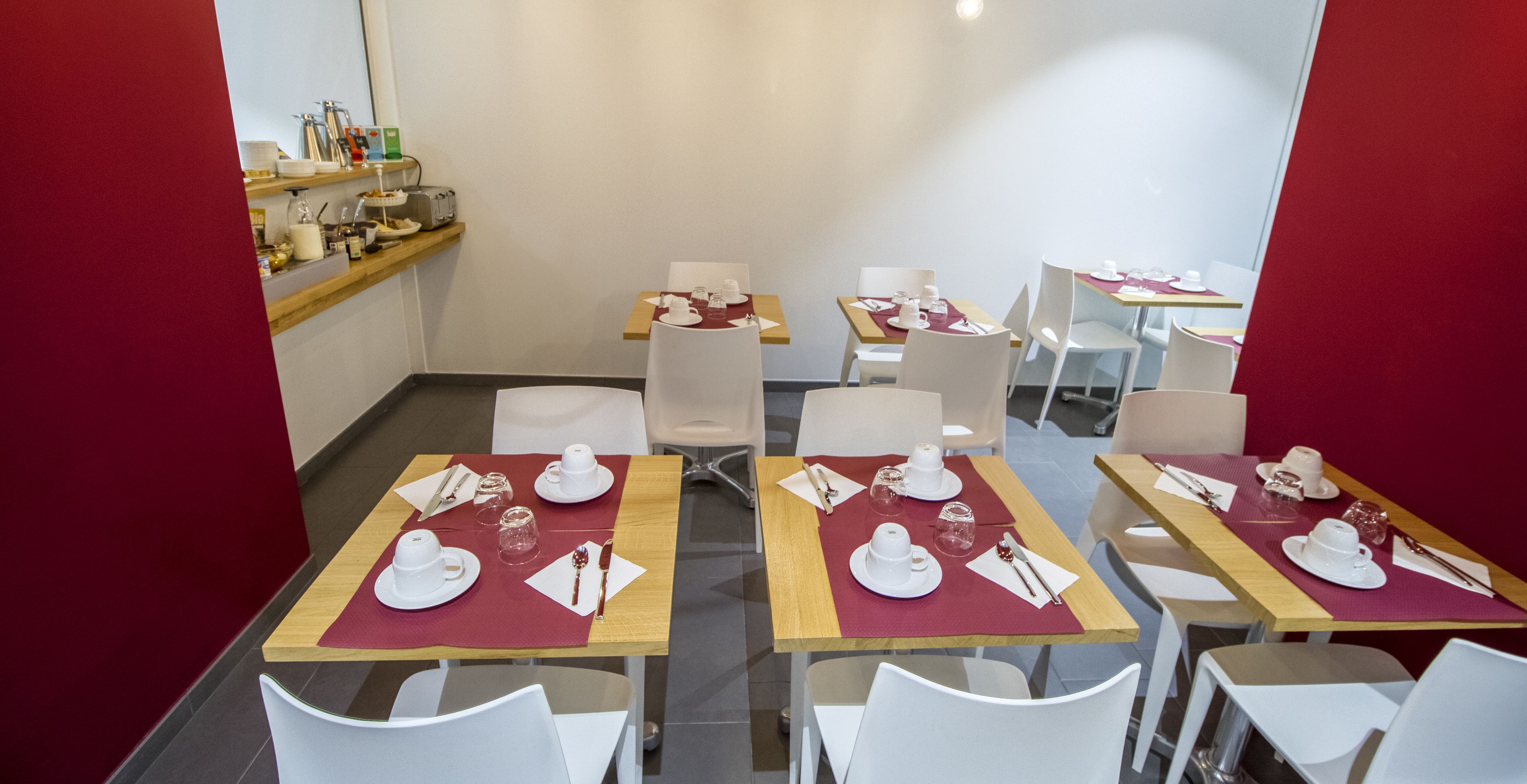 A dining area with tables set for four, each with white chairs, red placemats, and white tableware.