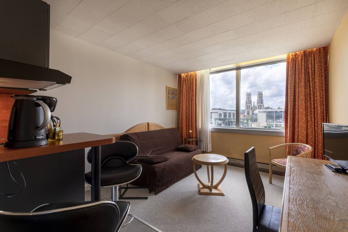 Una habitación de hotel con una cama, un escritorio, una silla, una mesita y un ventanal con cortinas.