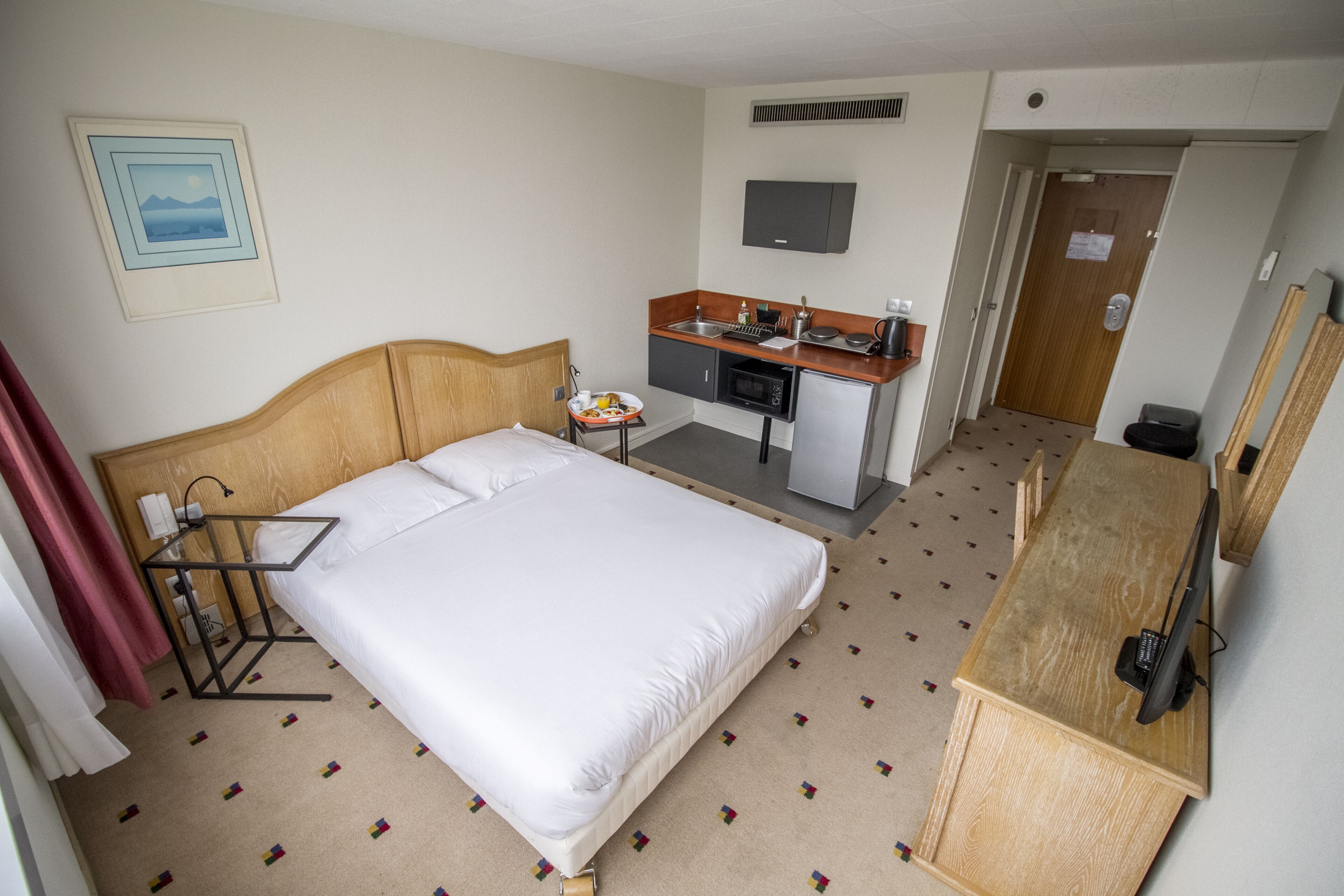 Una habitación de hotel con cama, kitchenette, televisión y puerta.