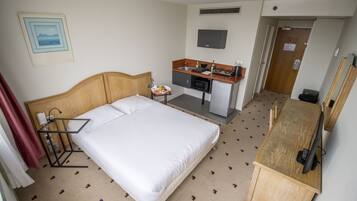 Una habitación de hotel con cama, kitchenette, televisión y puerta.