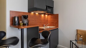A compact kitchen with a microwave, coffee maker, and sink. There are two black chairs and a glass table. - KOSY Appart'Hôtels - Coeur de Ville  (Nancy)