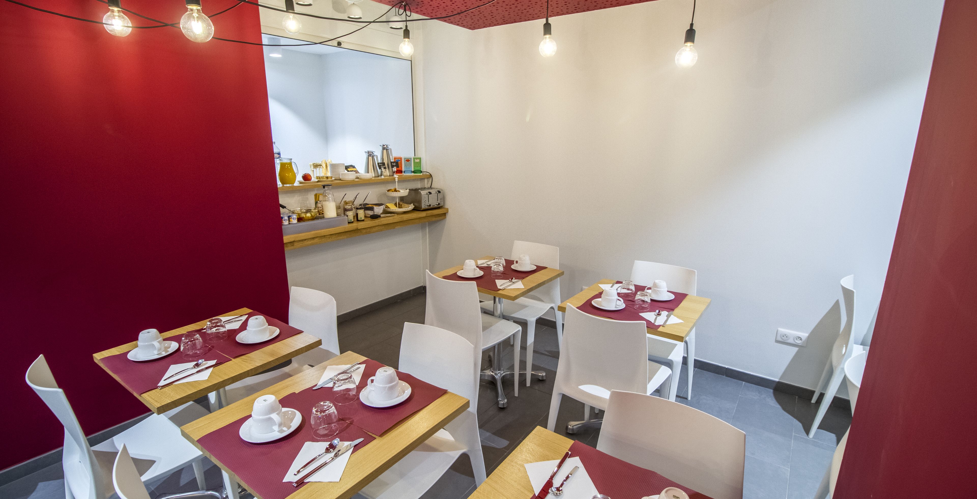 A modern dining area with tables set for four, white chairs, and a red accent wall.
