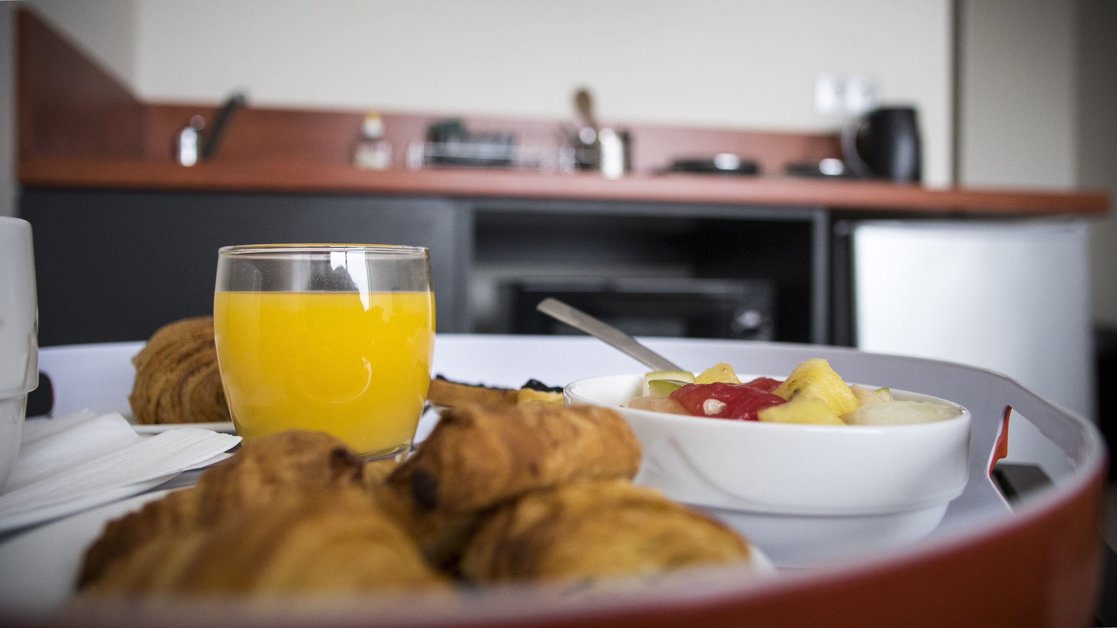 Un esmorzar amb croissants, un bol de fruita i un got de suc d'aranja sobre un safata.