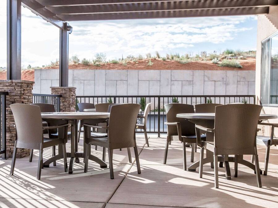 An outdoor patio with stone walls, wicker chairs, and tables, overlooking a desert landscape.