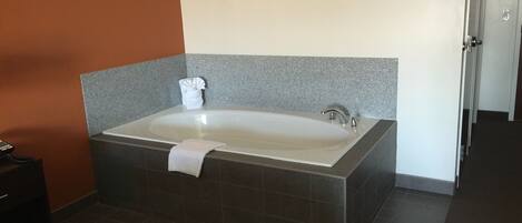 A modern bathroom with a large bathtub, a towel, and a small table with a bottle.