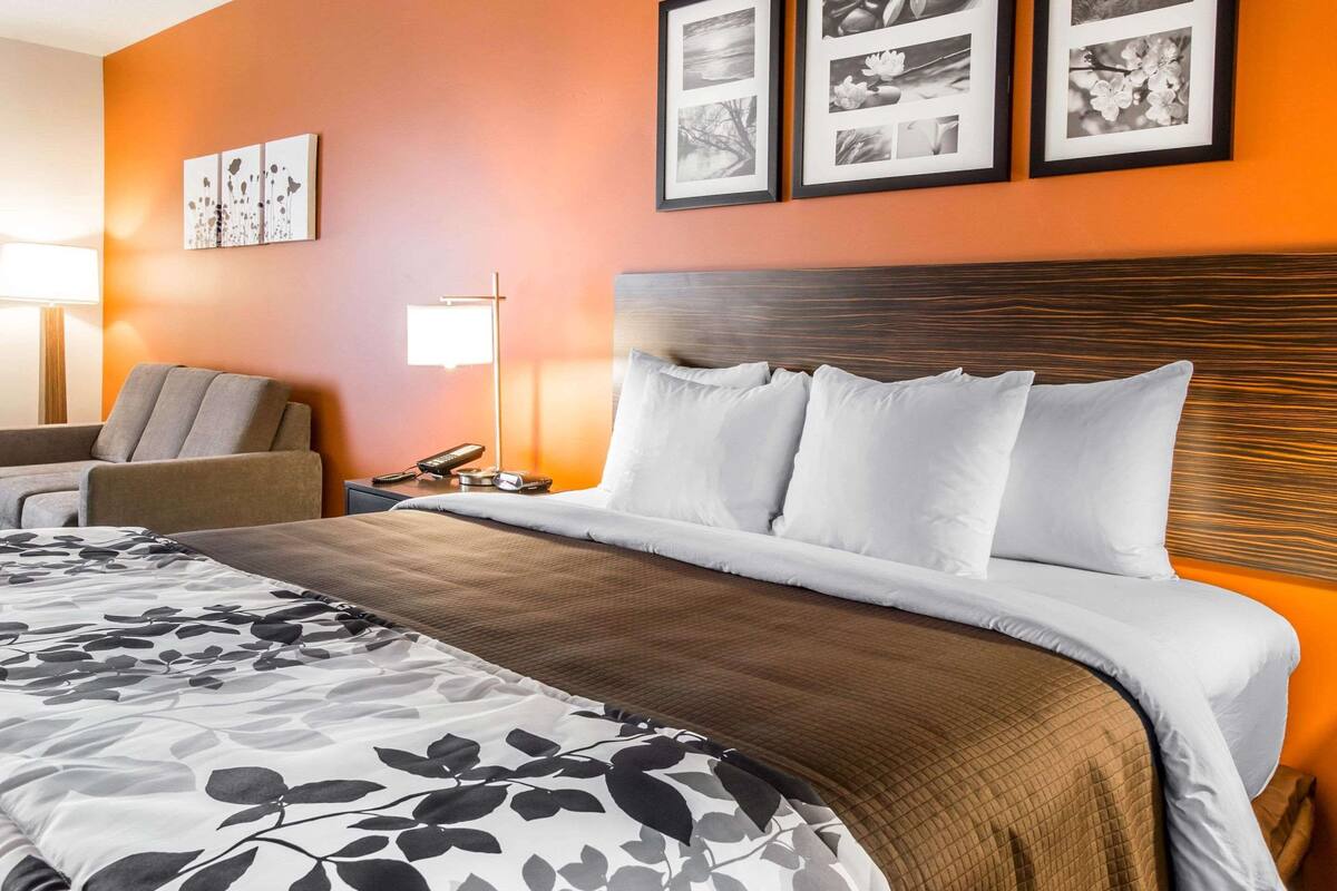 A hotel room with a large bed, a nightstand, a lamp, and a chair. There are three framed pictures on the wall above the bed.