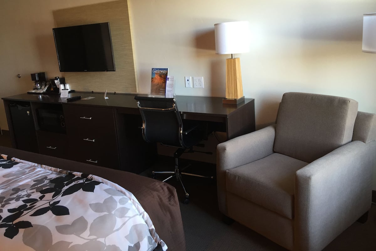 A hotel room with a bed, a desk, a chair, a TV, a lamp, and a sign on the wall.