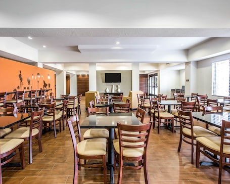 A spacious dining area with multiple tables and chairs, a flat-screen TV mounted on the wall, and a large orange mural on the left wall.