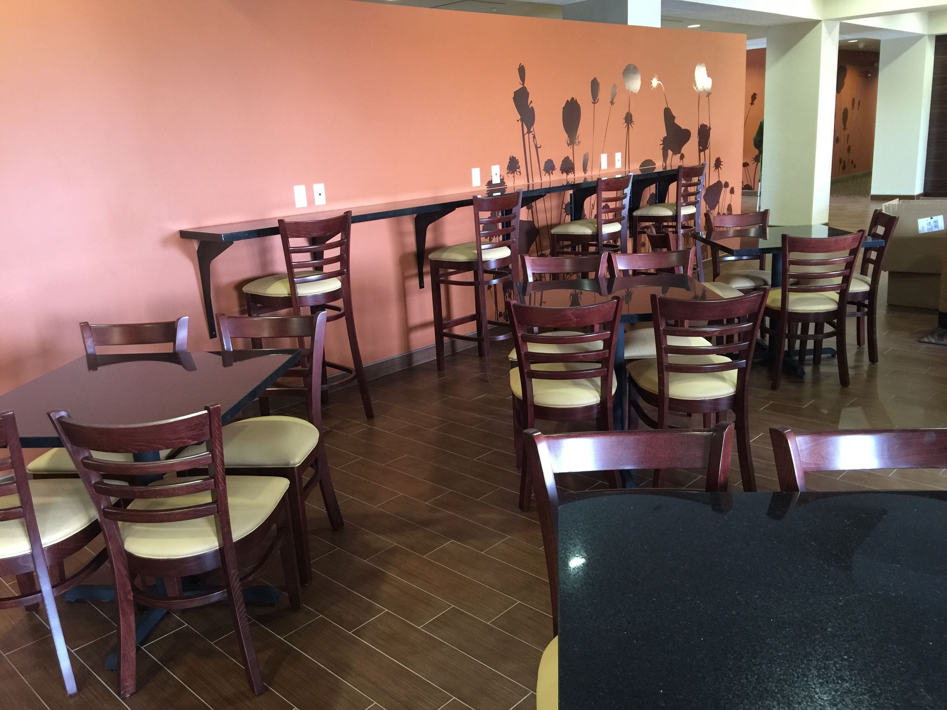 L’intérieur d’un restaurant présente de nombreuses tables et chaises en bois, un mur de couleur pêche orné d’une fresque florale et un sol carrelé.