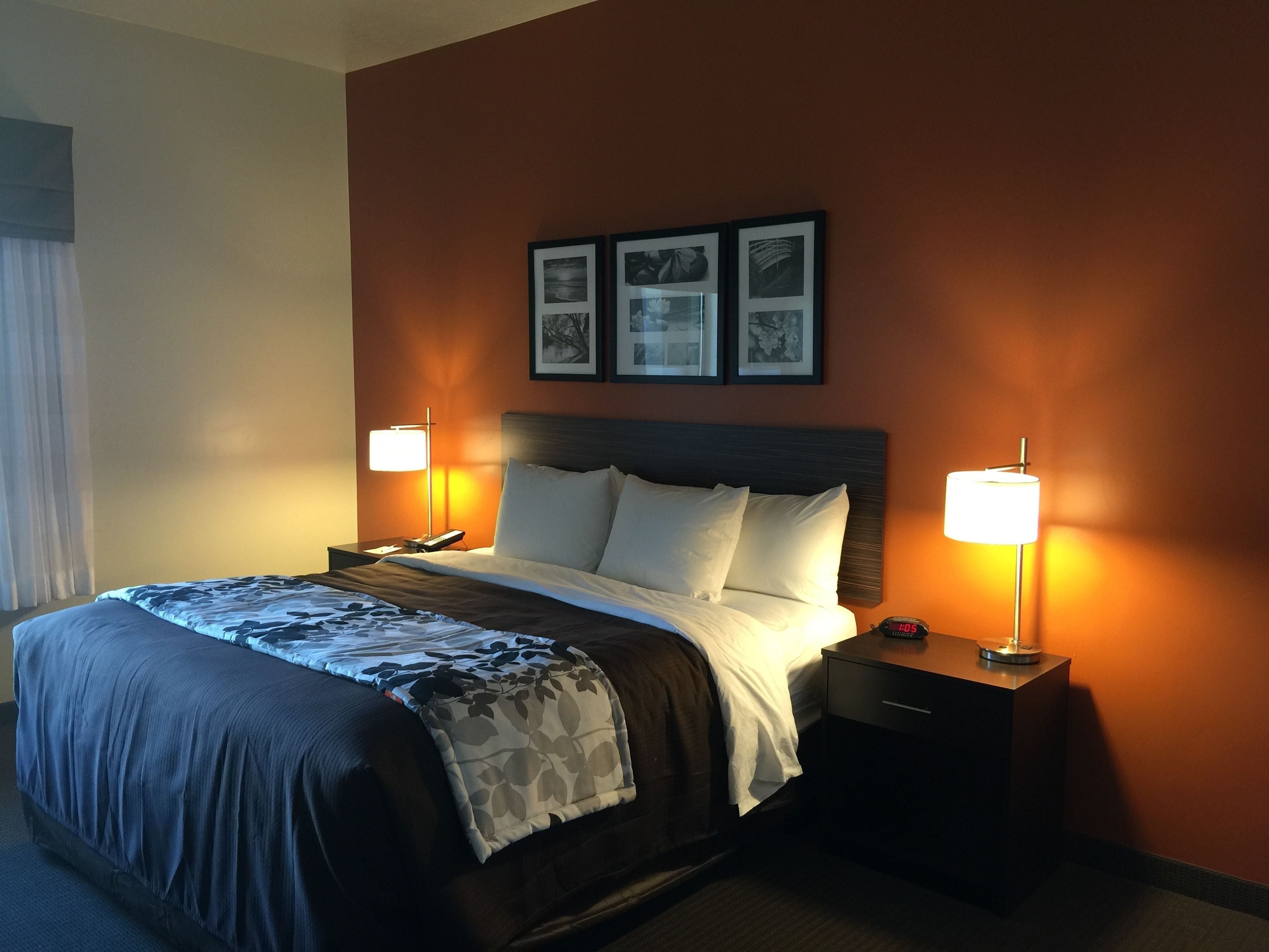 A hotel room with a large bed, two bedside tables with lamps, a nightstand, and framed pictures on the wall.