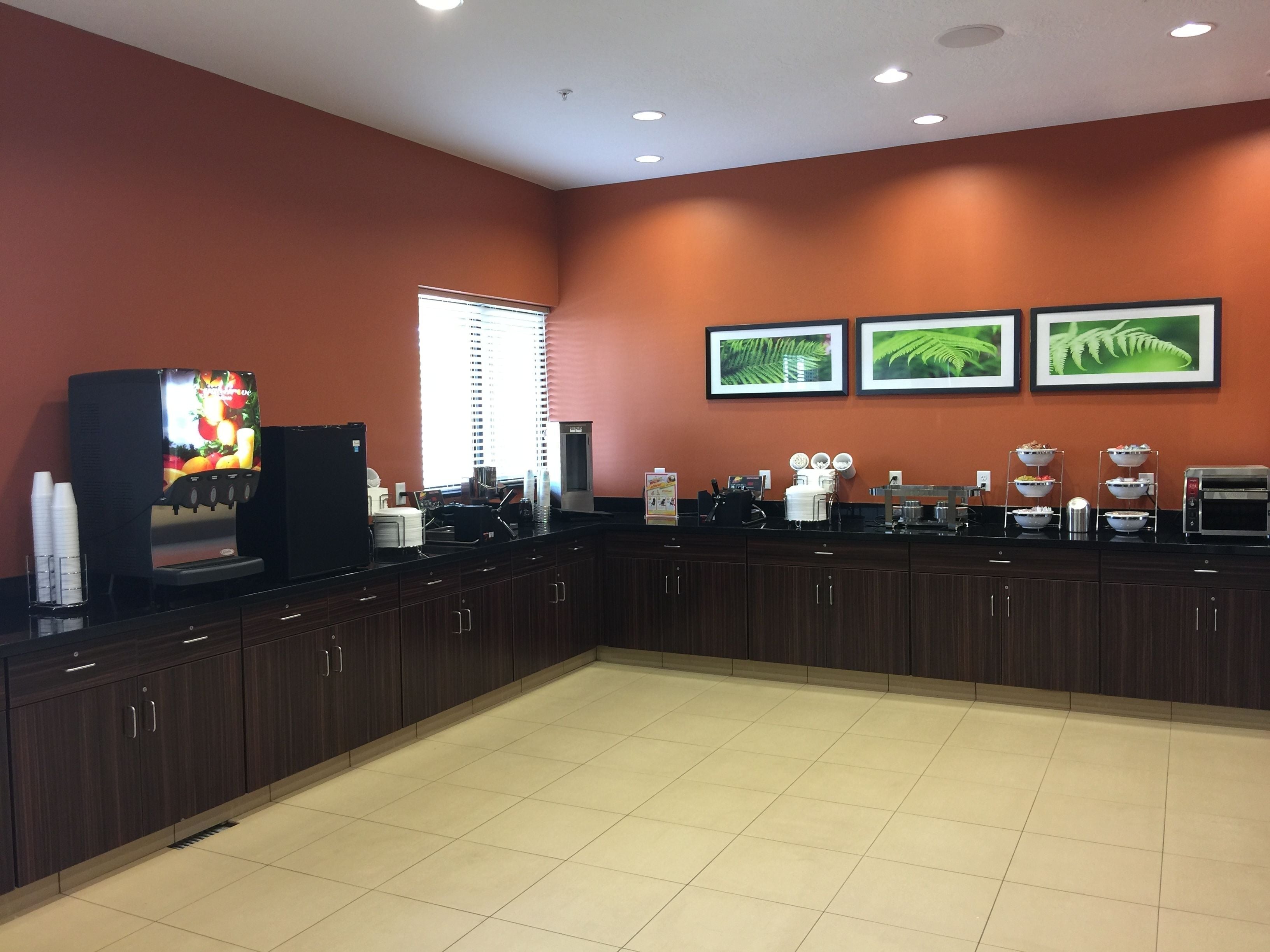 A kitchen with dark wooden cabinets, a black countertop, a coffee machine, a toaster, and a refrigerator. There are three framed pictures on the wall.