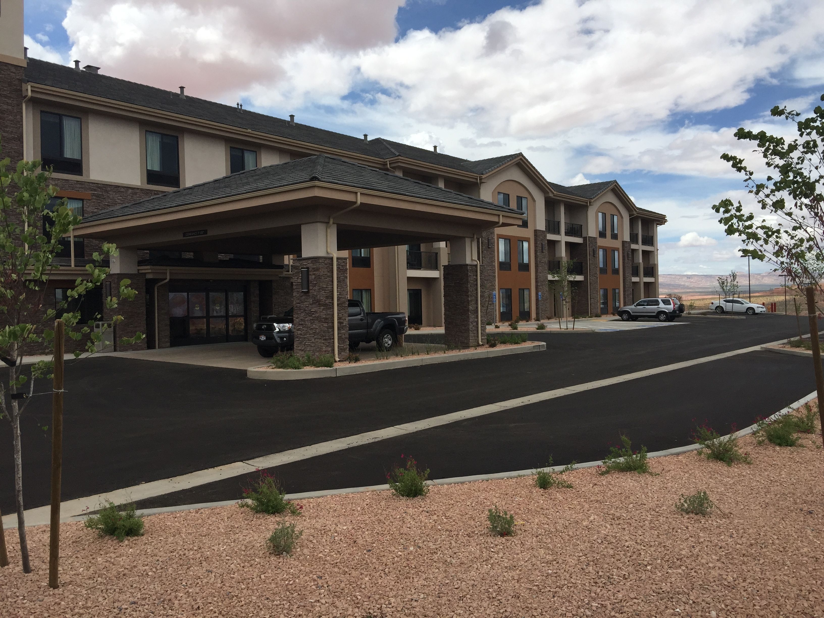 A multi-story hotel with a covered entrance, parking area, and a view of the surrounding landscape.