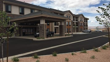 Un hotel de varios pisos con entrada cubierta, zona de estacionamiento y vistas del paisaje circundante.