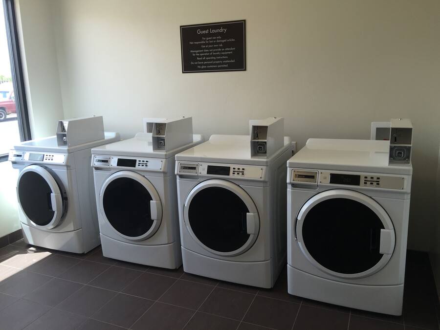 A row of four front-loading washing machines in a laundry room with a sign above them.