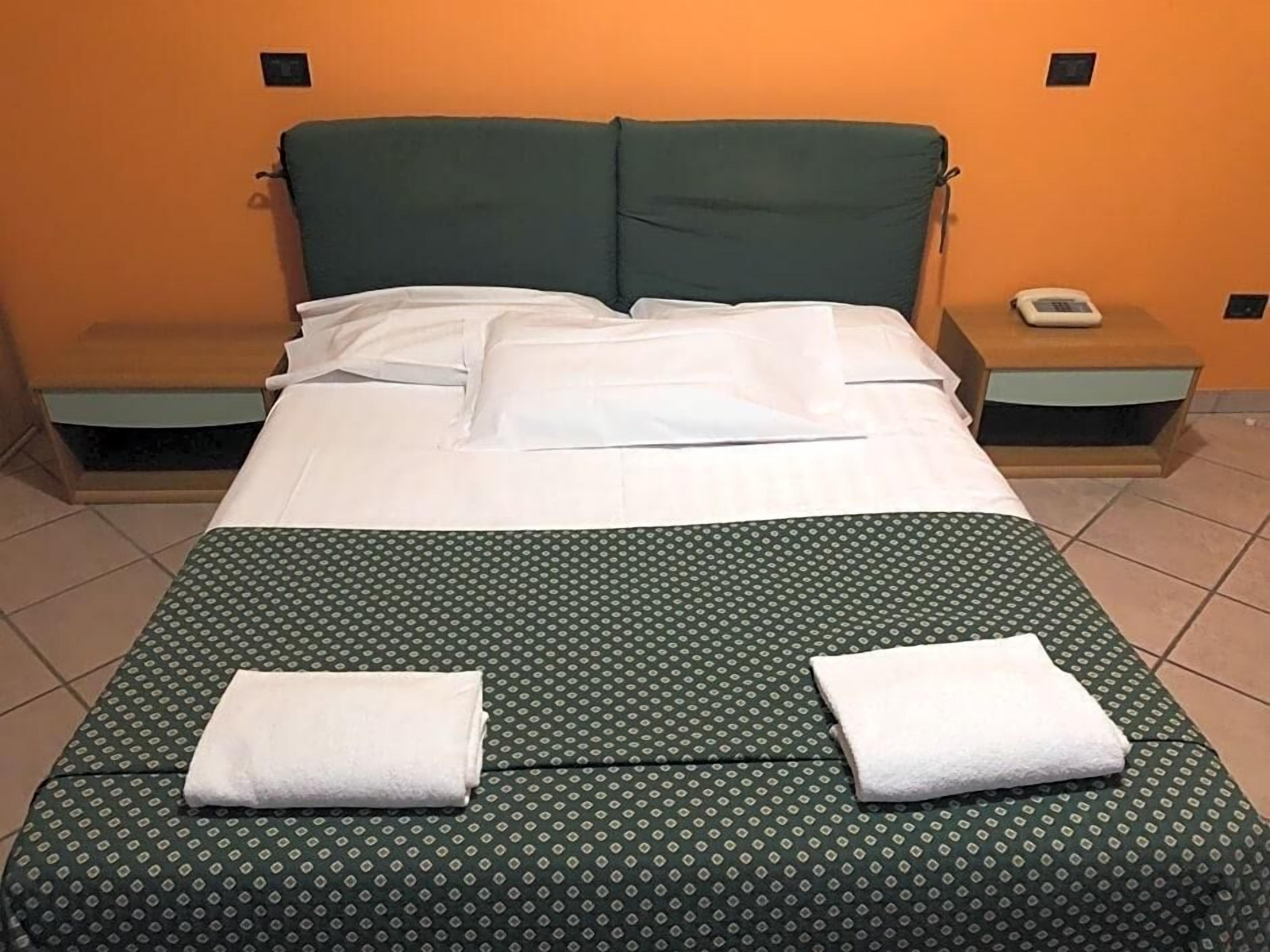 Una cama con una colcha verde estampada, dos almohadas blancas y dos toallas blancas dobladas sobre la cama.