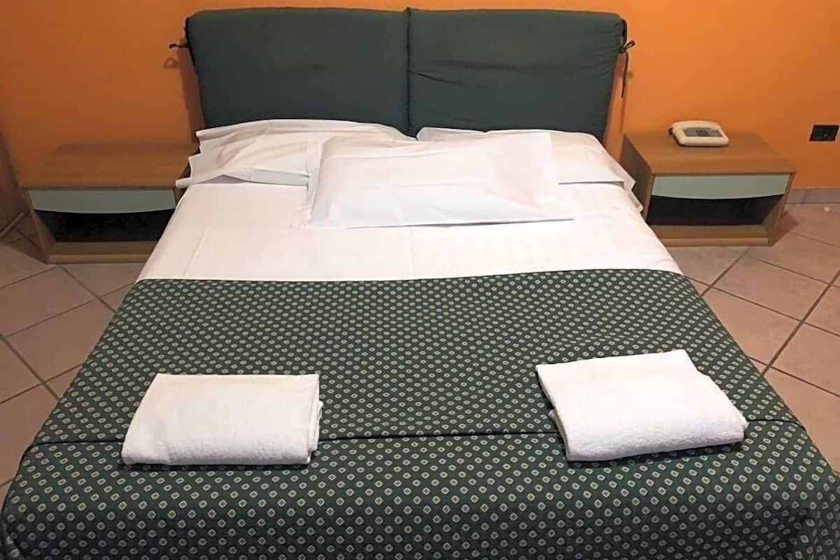 Una cama con una colcha verde estampada, dos almohadas blancas y dos toallas blancas dobladas sobre la cama.
