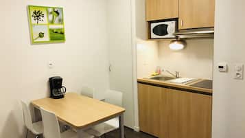 Una cocina compacta con microondas, fregadero y cafetera sobre la encimera. Hay una mesa de comedor con sillas y un cuadro colgado en la pared.
