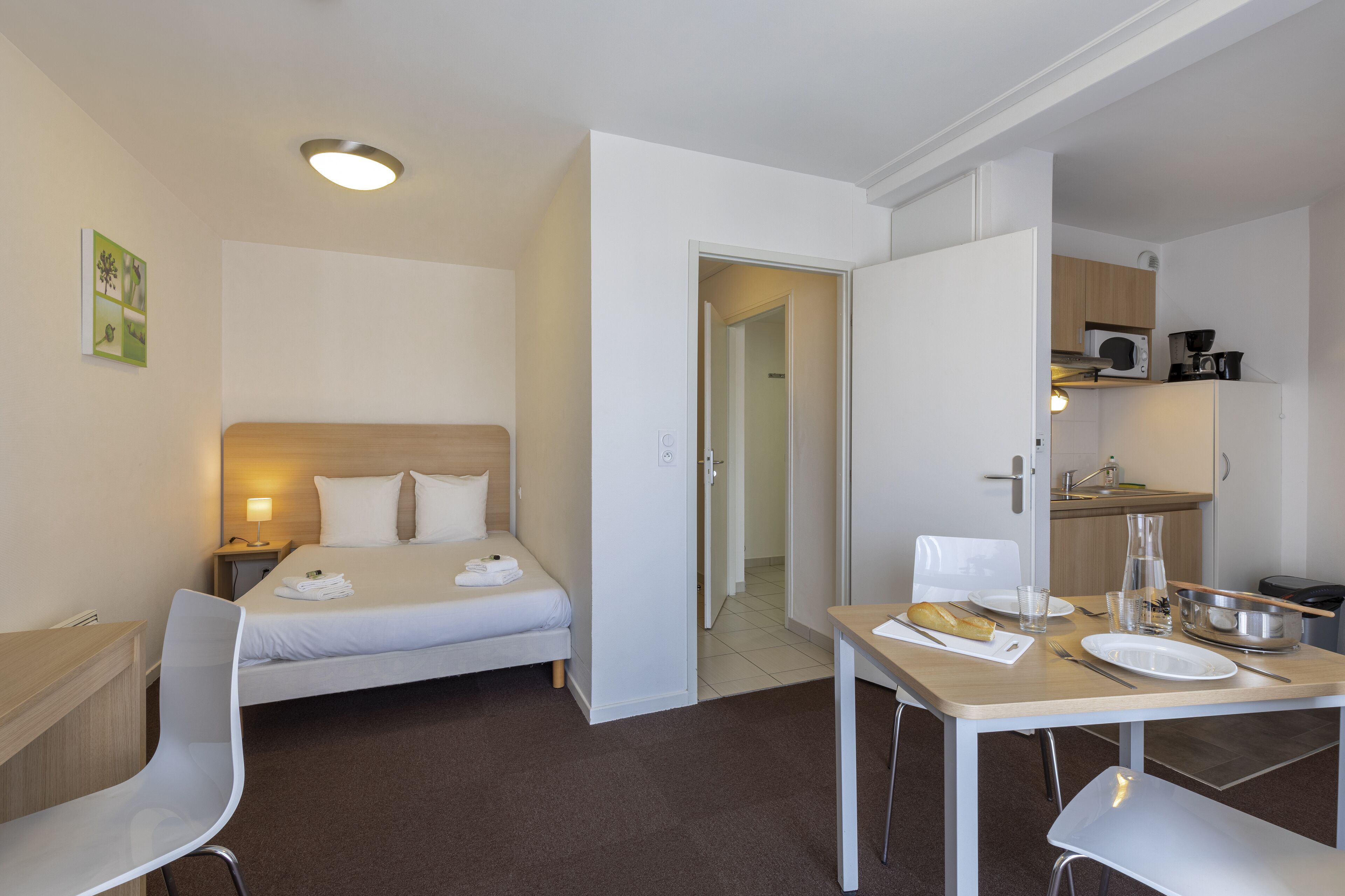 Een hotelkamer met een bed, een bureau, een stoel, een tafel en een kitchenette.