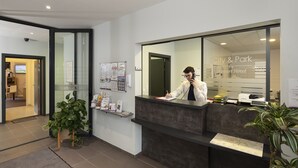 A hotel reception desk with a receptionist, a map, and informational posters on the wall. - KOSY Appart'Hôtels Troyes - City & Park (Troyes)